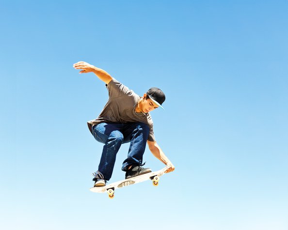 A young white man wearing a baseball cap and doing a jump trick on a skateboard.